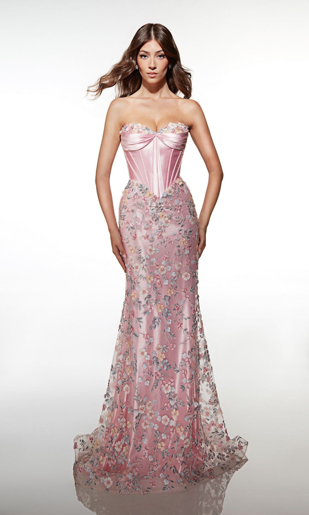 A woman poses against a plain white background wearing the Alyce 62197 long prom dress—a strapless pink gown featuring a corset bodice and delicate 3D floral embellishments.